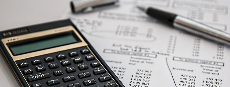 Ein Taschenrechner, ein Stift und ein Blatt Papier mit Statistiken liegen auf einem Tisch.