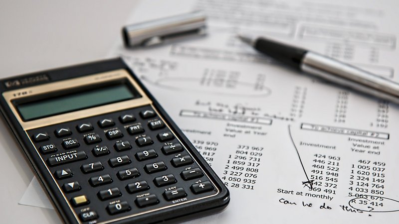 Ein Taschenrechner, ein Stift und ein Papier mit Statistiken liegen auf einem Tisch.