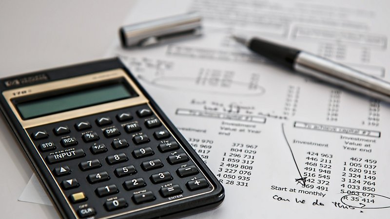 Symbolbild: Auf einem Tisch liegen ein Taschenrechner, ein Papier mit Statistiken und ein Kugelschreiber