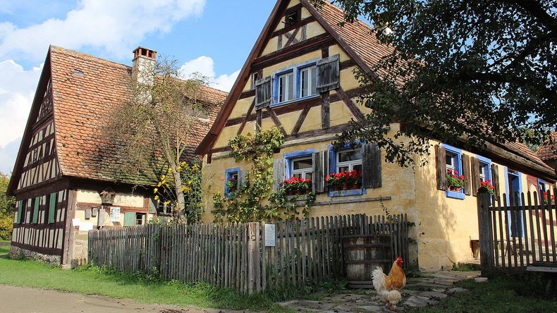 Zwei alte Fachwerkhäuser-Bauernhäuser im Freilandmuseum, sie sind umgeben von Bauerngärten, der Himmel ist blau. 