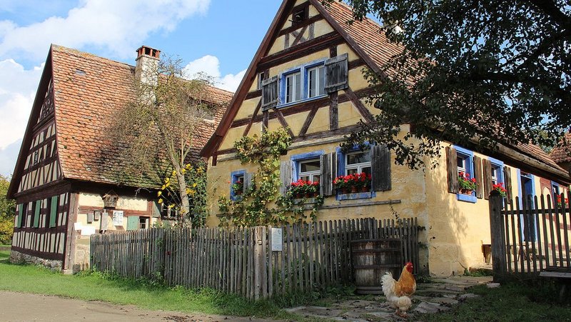 Zwei alte Fachwerkhäuser-Bauernhäuser im Freilandmuseum, sie sind umgeben von Bauerngärten, der Himmel ist blau. 