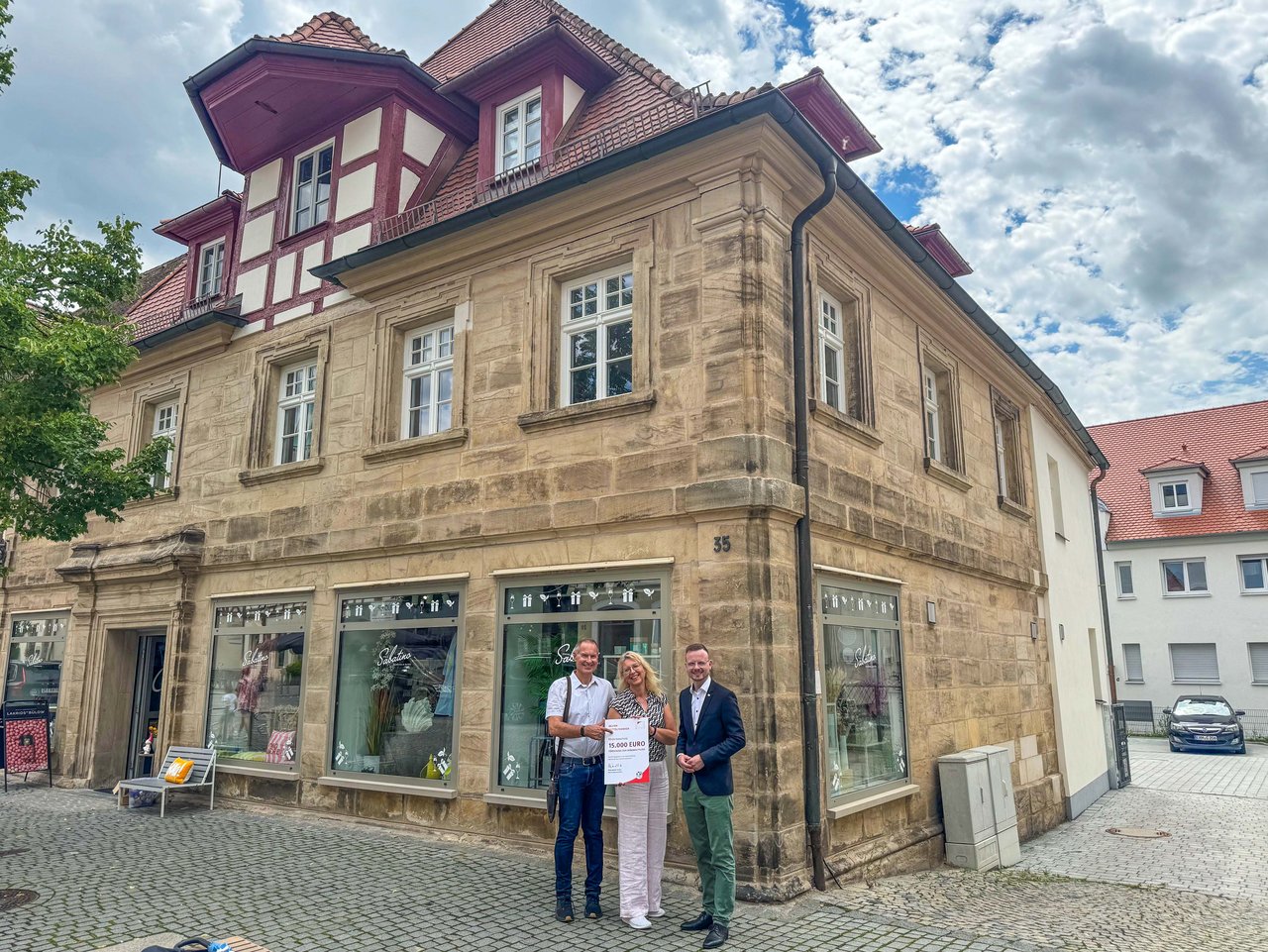 Bezirkstagspräsident Peter Daniel Forster überreicht vor dem sanierten Gebäude in Herzogenaurach den Förderbescheid zur Förderung der Denkmalpflege an Manuela Janisch und Gerd Gumbrecht.