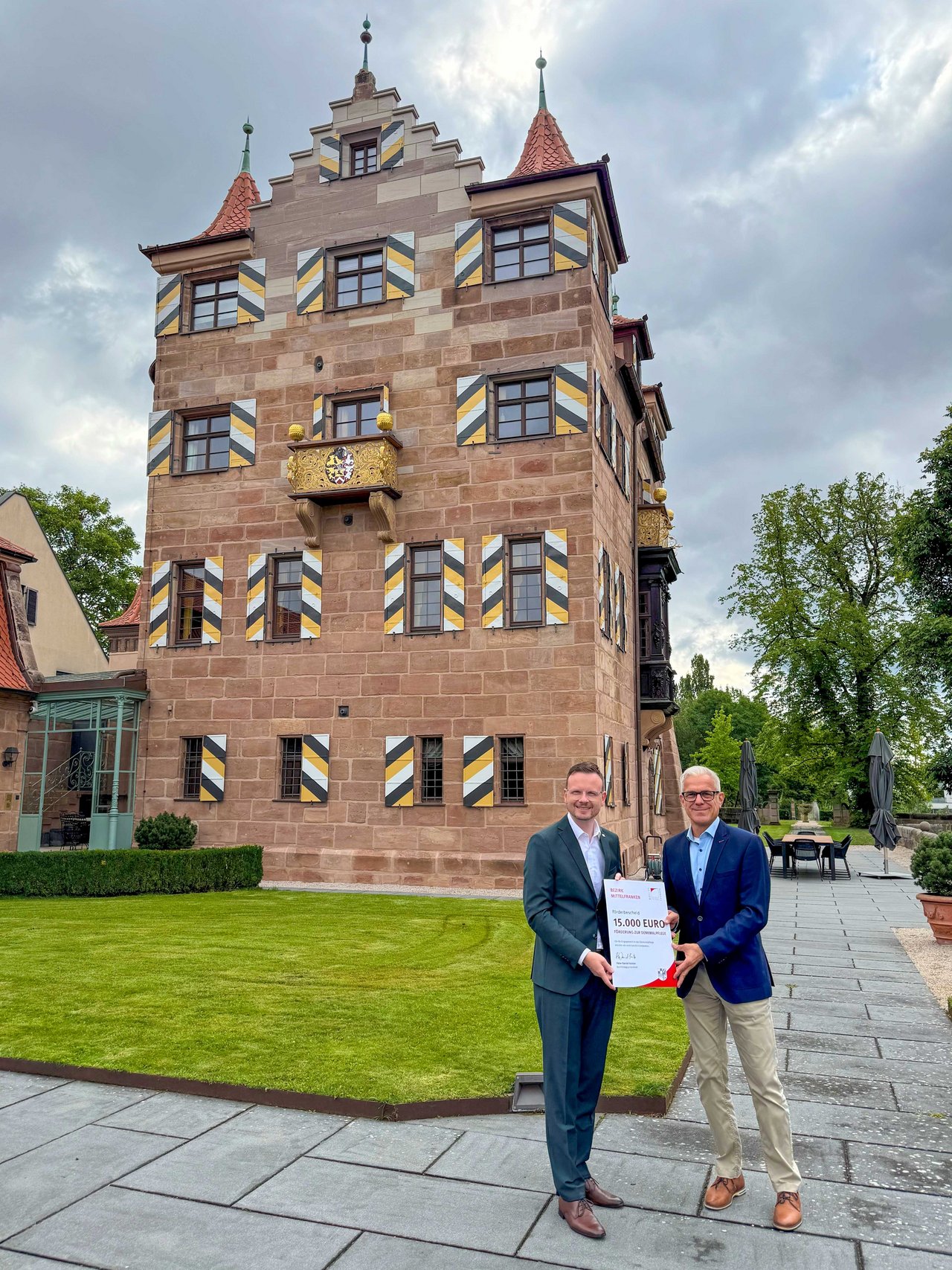 Vor dem Herrensitz Schoppershof überreicht Bezirkstagspräsident Peter Daniel Forster einen Förderbescheid an Jens Hinkelmann, Mitglied der Geschäftsleitung der Dr. Lorenz Tucher’sche Stiftung.
