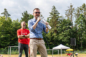 Bezirkstagspräsident Peter Daniel Forster steht auf einem Sportplatz und spricht gerade in ein Mikrofon.