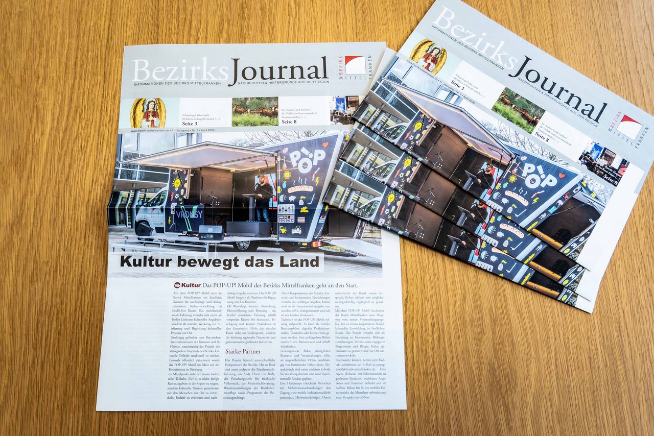 Mehrere Ausgaben der aktuellen Ausgabe des Bezirks-Journals liegen aufeinander auf einem Tisch. Daneben liegt eine Ausgabe, von der die Titelseite aufgeschlagen ist.