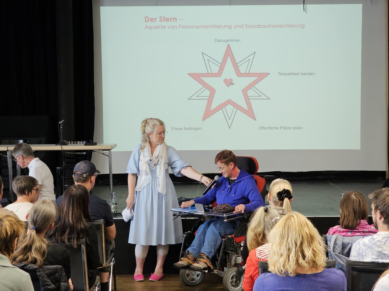 Sabrina Wölfel sitzt in einem Rollstuhl und spricht zum Publikum.