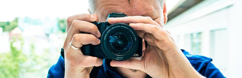 Ein Mann mit Kamera in der Hand fotografiert gerade in Richtung des Zuschauers.