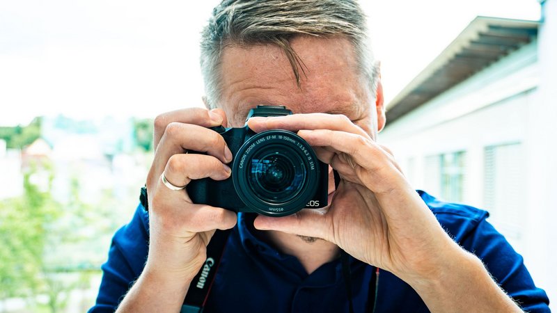 Ein Mann mit Kamera in der Hand fotografiert gerade in Richtung des Zuschauers.