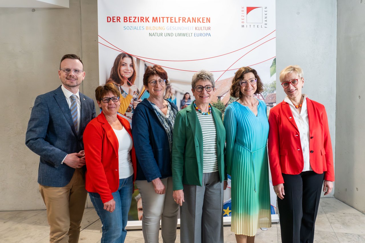 Die genannten Personen stehen für ein Gruppenbild vor einem Bezirks-Rollup im Bezirksrathaus.
