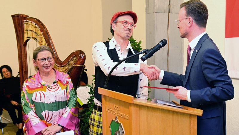 Bezirkstagspräsident Peter Daniel Forster schüttelt einem Künstler am Podium gerade bei der Preisübergabe die Hand.
