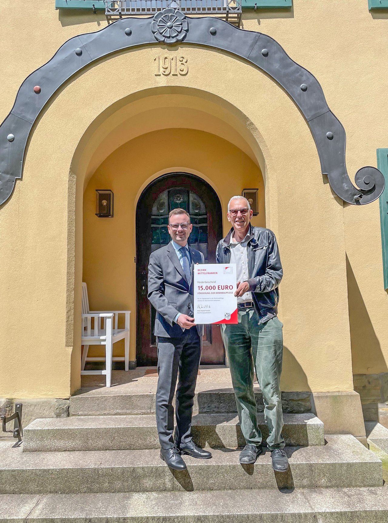 Bezirkstagspräsident Peter Daniel Forster (l.) überreicht den Förderbescheid des Bezirks Mittelfranken an Heinrich Klotz (r.)