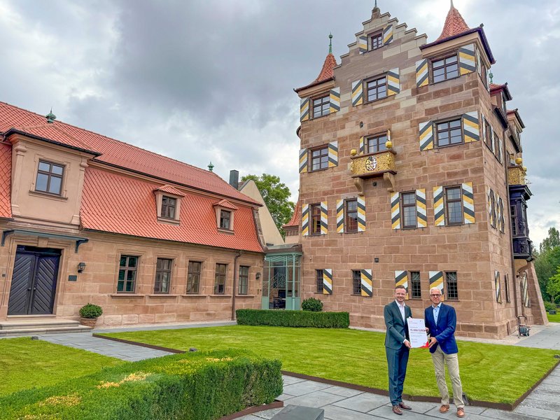 Vor dem Herrensitz Schoppershof überreicht Bezirkstagspräsident Peter Daniel Forster einen Förderbescheid an Jens Hinkelmann, Mitglied der Geschäftsleitung der Dr. Lorenz Tucher’sche Stiftung.
