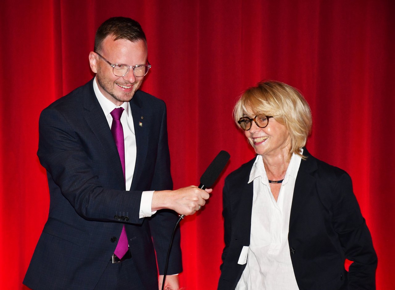 Peter Daniel Forster hält Gisela Schneeberger auf der Bühne ein Mikrofon hin.
