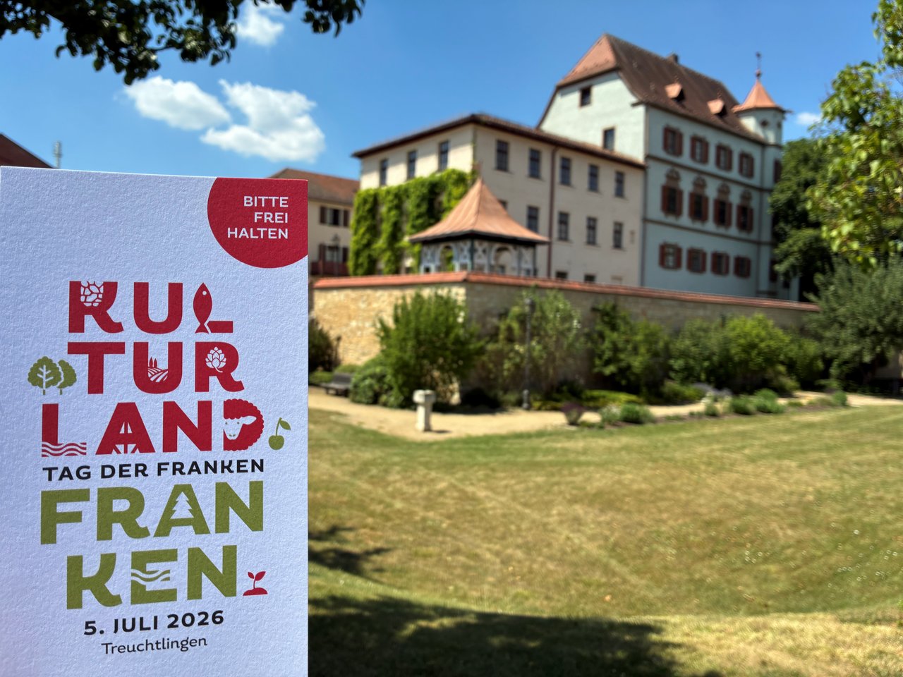 Foto des Schlosses in Treuchtlingen. Links daneben wird der Flyer des Tags der Franken in die Kamera gehalten.