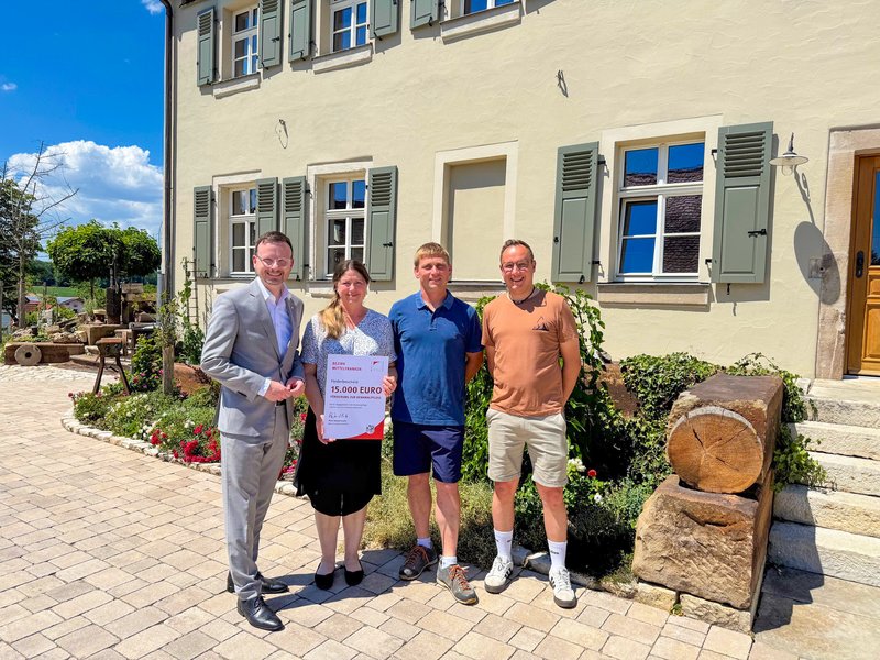 Die aufgezählten Leute stehen für ein Gruppenbild vor dem sanierten Gebäude und halten dabei die überreichte Urkunde hoch.
