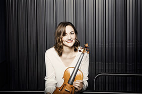 Franziska Hölscher mit Geige vor einem dunklen Vorhang. 