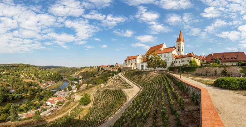 Ein Blick von einem Berg auf eine auf dem Berg gelegene Kirche. Links kann man ins Tal blicken. Auf den Hängen befinden sich zahlreiche Weinberge.