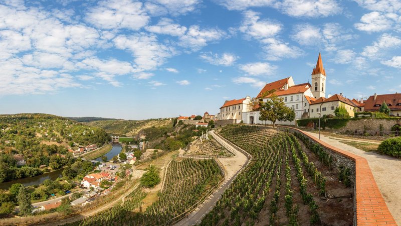 Ein Blick von einem Berg auf eine auf dem Berg gelegene Kirche. Links kann man ins Tal blicken. Auf den Hängen befinden sich zahlreiche Weinberge.