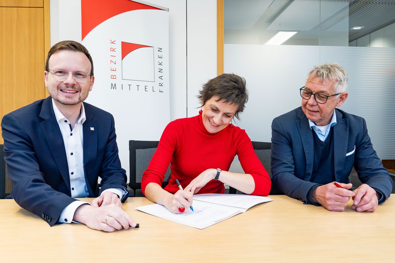 Drei Personen sitzen am Tisch zur Vertragsunterzeichnung