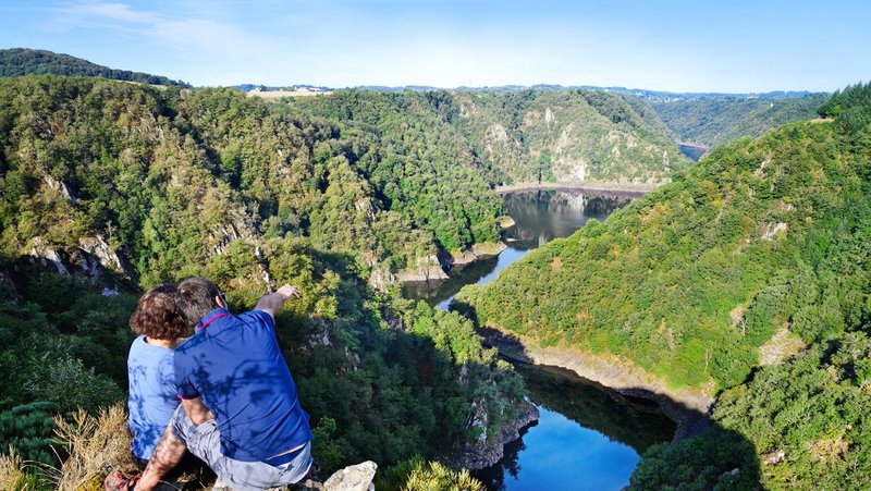 Zwei Menschen sitzen auf einem Berg und schauen ins Tal. Durchs Tal schlängelt sich ein Fluss.