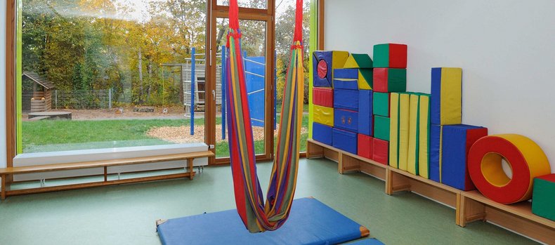 Blick in ein Spielzimmer einer Schule. Es liegen Sportmatten auf dem Boden, in der Mitte des Raums hängt eine kleine Hängematte.