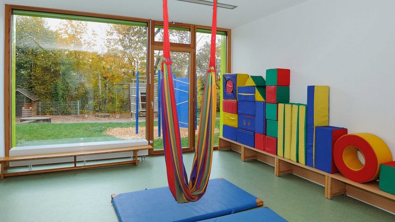 Blick in ein Spielzimmer einer Schule. Es liegen Sportmatten auf dem Boden, in der Mitte des Raums hängt eine kleine Hängematte.