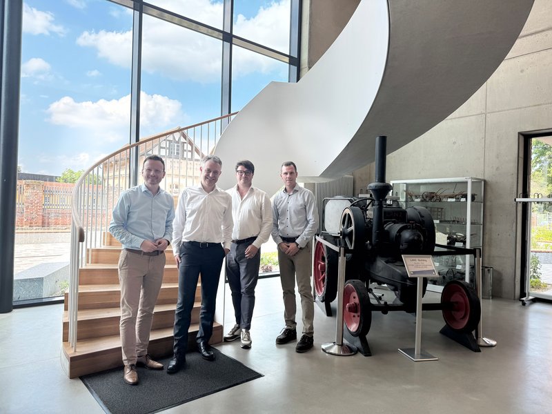 Peter Daniel Forster, Dr. Thomas Koch, Daniel Goltz und Markus Heinz stehen in einem Gebäude in Triesdorf für ein Gruppenfoto vor einer Wendeltreppe. Im Hintergrund steht auch ein historischer Traktor.