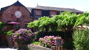 Foto eines französischen Backsteinhauses mit einem bunt blühendem Vorgarten.