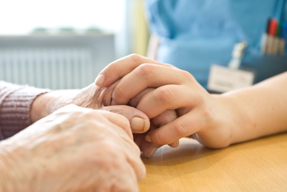 Eine jüngere Hand hält eine ältere Hand fest, die auf einem Tisch liegen.